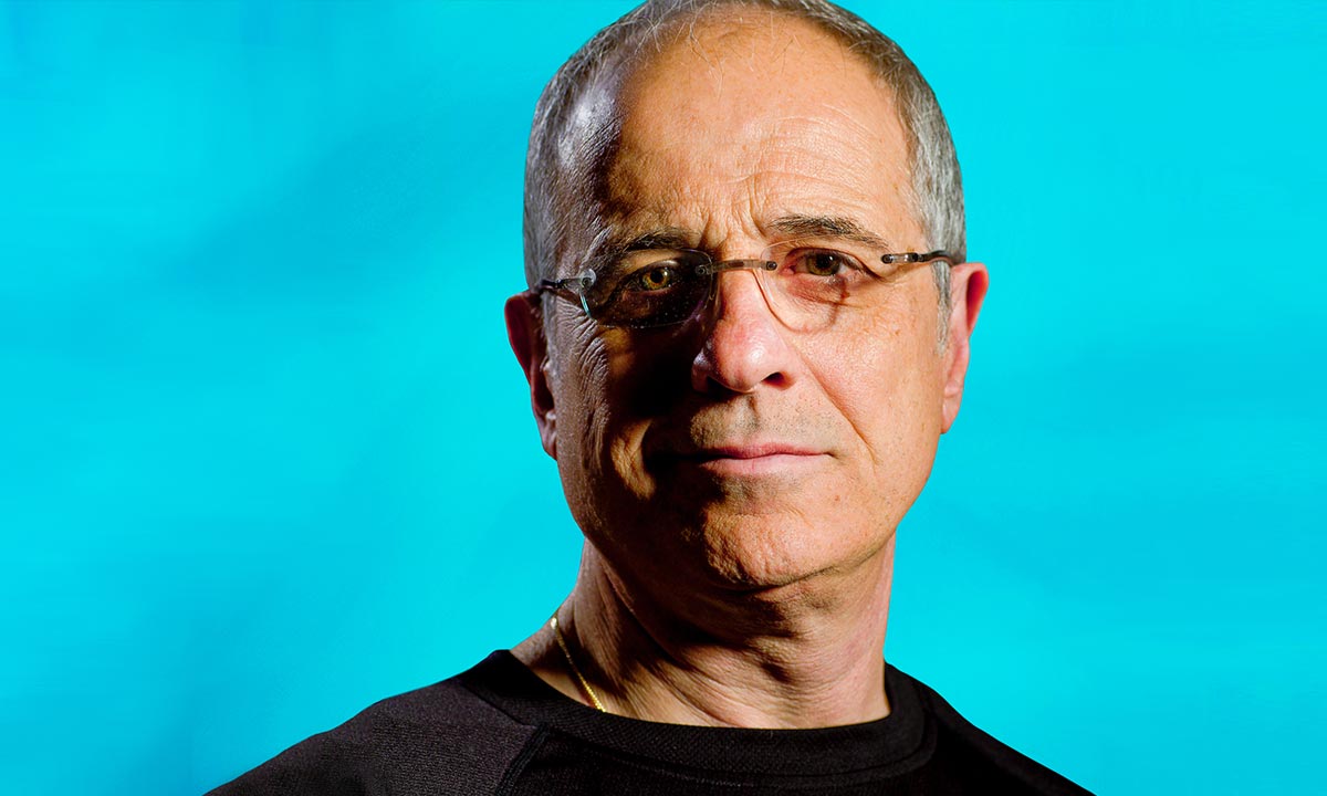 man with an aqua background with eye glasses and a solemn look